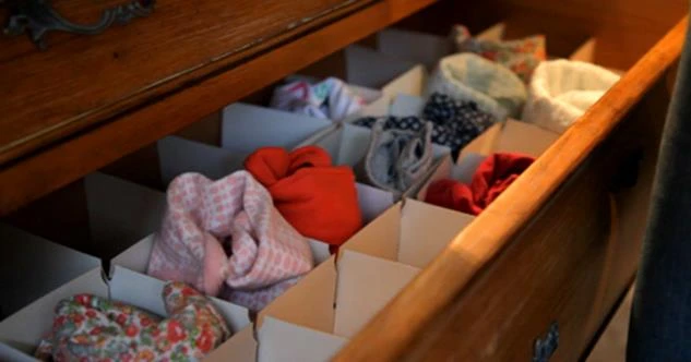 An open dresser drawer showing baby onesies separated by dividers