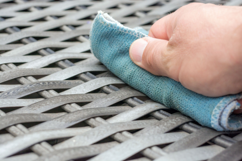 Person wiping wicker patio furniture with microfiber cloth