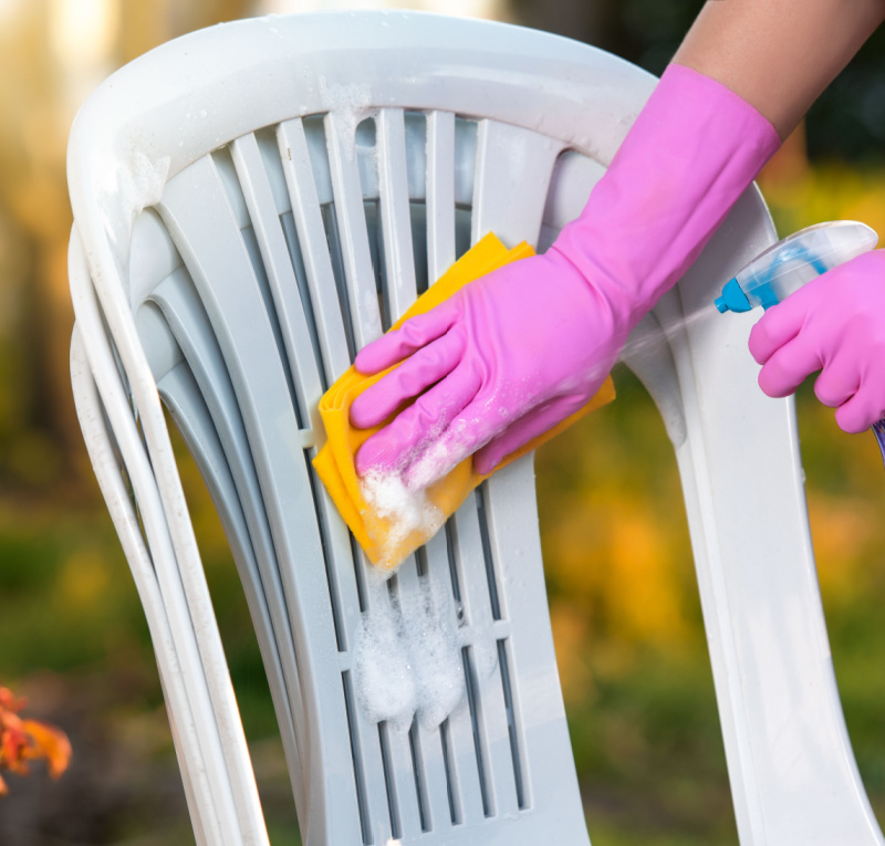 Person cleaning plastic patio chairs with a sponge