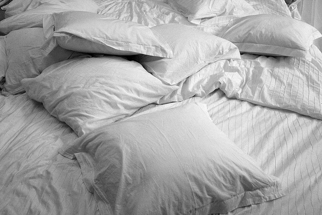 White pillows tossed on a bed with a white duvet cover. Photo Cred: Luc De Leeuw on Flickr.