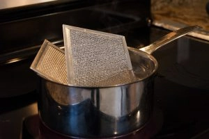 Two dirty range-hood filters in a pot of water on a stove