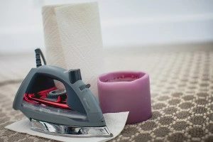 A purple candle, roll of paper towels, and an iron on beige-patterned carpet