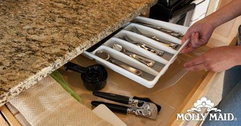A person organizing a kitchen drawer containing silverware in a tray and utensils