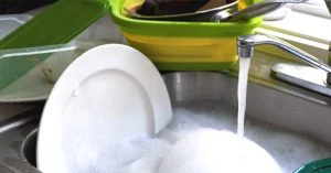 White dishes in a kitchen sink with soapy water and the faucet turned on