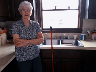 Grandmotherly figure standing in the kitchen with arms crossed