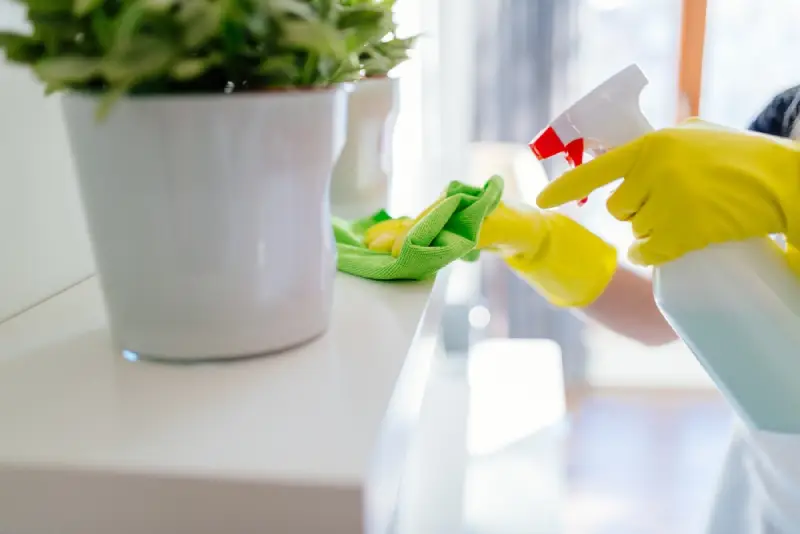Person in yellow rubber gloves cleaning a cleaning white shelf.