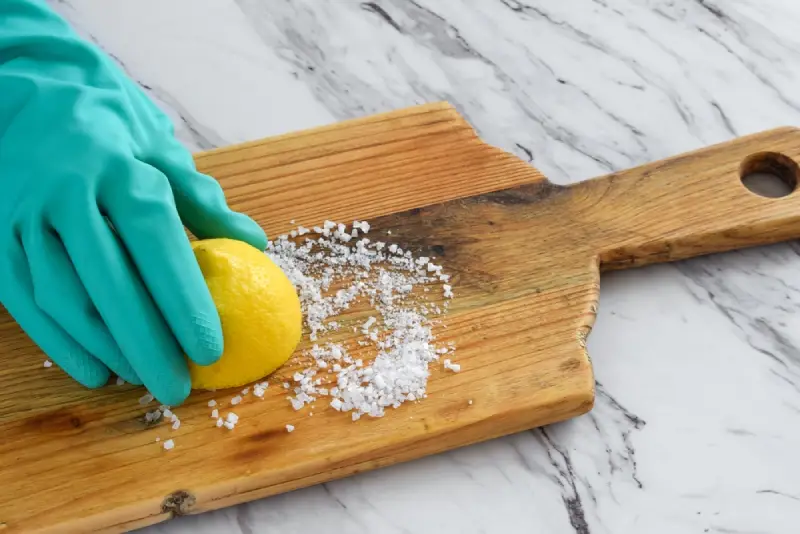 Closeup of person’s hand in protective rubber glove scrubbing wooden cutting board with lemon juice and salt