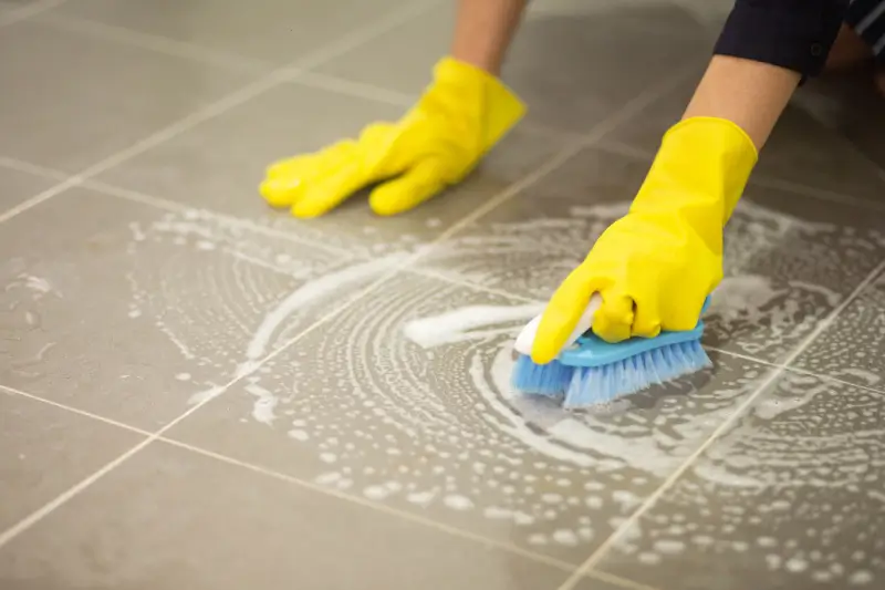 House cleaner scrubbing stain on tile floor with a brush.