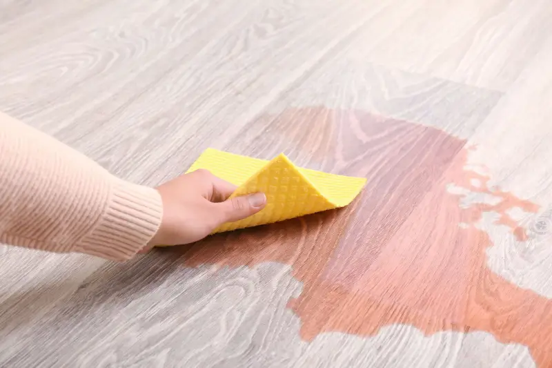 Person wiping up wine spill on wood floor.