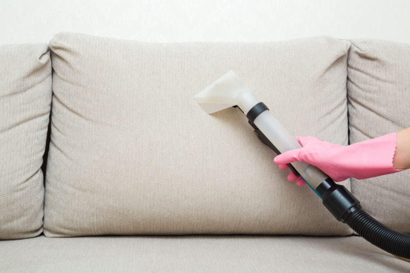 Person using vacuum on fabric couch