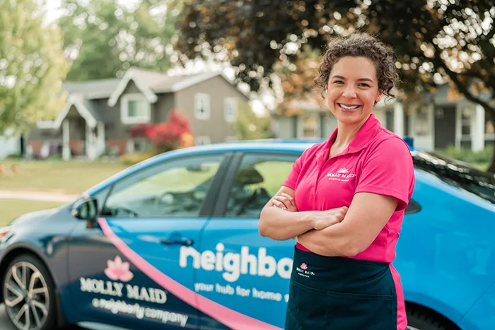A Molly Maid professional standing by a company car and smiling before a cleaning service appointment